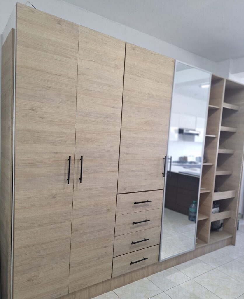 Closet de piso a techo en roble claro con puertas batientes, cajonera, puerta con espejo y repisas abiertas