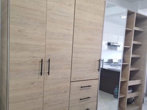 Closet de piso a techo en roble claro con puertas batientes, cajonera, puerta con espejo y repisas abiertas