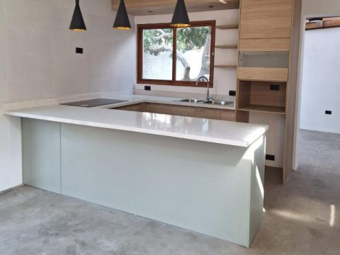 Cocina con barra en verde suave, muebles en madera clara y lámparas colgantes