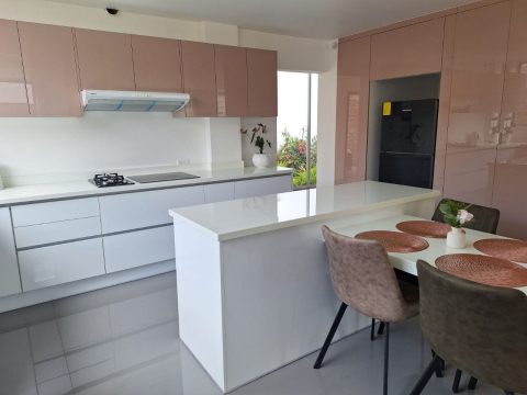 Cocina con muebles altos lacados en rosa, muebles bajos blancos e isla con comedor