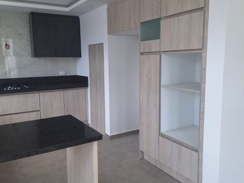 Muebles altos y alacena en madera clara con nicho abierto e isla de granito negro